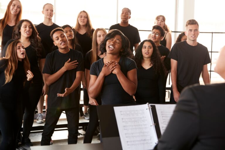 Male And Female Students Singing In Choir With Teacher At Performing Arts School